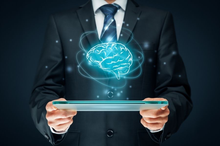 A businessman holding a glass tablet with a glowing blue brain hologram above it for a beginners machine learning guide.
