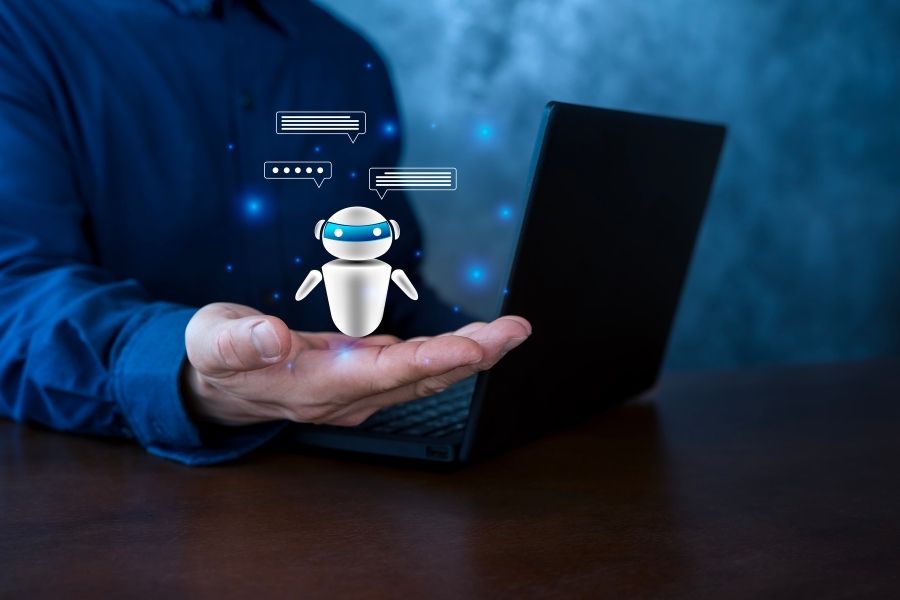 A small robot hologram floats above a hand near a laptop to showcase AI copywriting software.