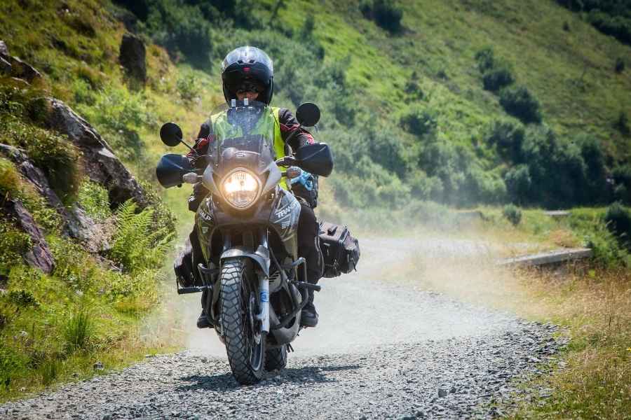 A rider on an adventure motorcycle equipped with protective motorcycle screens navigating a gravel path.