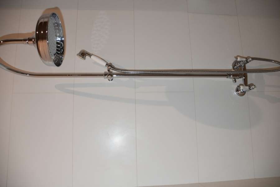 A modern chrome shower system mounted against a white tiled wall, featuring a large overhead shower and an attached handheld wand.