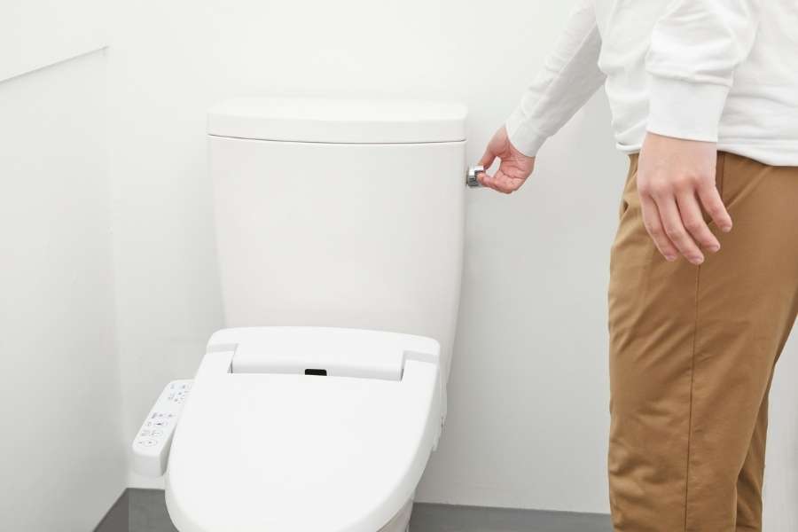 A man pushing the flush handle of a modern white toilet with an electronic bidet seat.